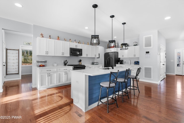 kitchen featuring white cabinetry, dark hardwood / wood-style flooring, hanging light fixtures, a kitchen island with sink, and black appliances