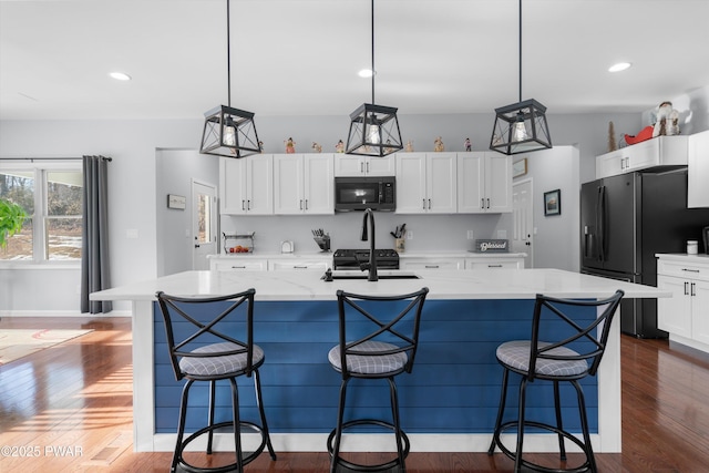 kitchen with light stone counters, decorative light fixtures, a kitchen island with sink, and black appliances