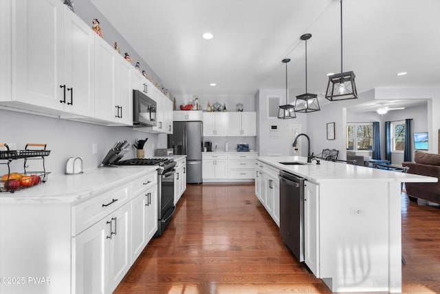 kitchen with appliances with stainless steel finishes, white cabinetry, an island with sink, sink, and hanging light fixtures