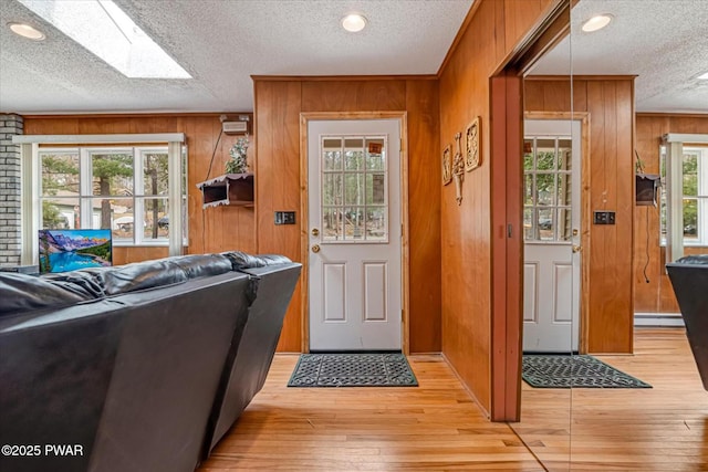 111 N Redwood Dr, Greentown, PA 18426 - doorway to outside featuring a textured ceiling, a skylight, wooden walls, a baseboard radiator, and light wood-style flooring