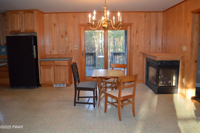 dining room featuring visible vents, wood walls, light floors, a fireplace, and a notable chandelier