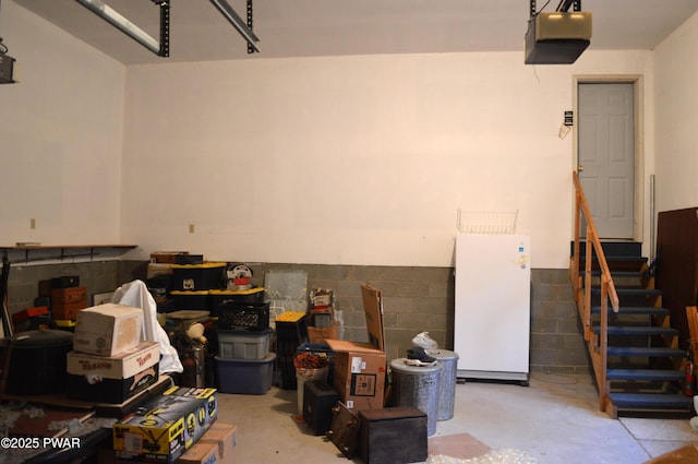 garage with a garage door opener, concrete block wall, and freestanding refrigerator