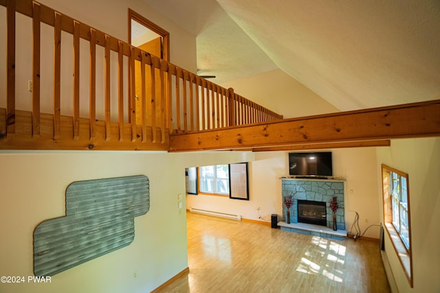 living room with a stone fireplace, high vaulted ceiling, light wood-type flooring, and a baseboard heating unit