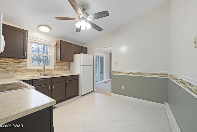 kitchen featuring dark brown cabinetry, sink, vaulted ceiling, and white fridge