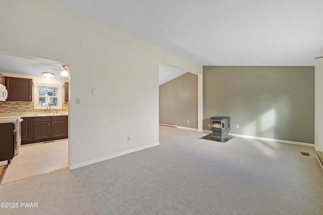 unfurnished living room with vaulted ceiling, sink, a wood stove, ceiling fan, and light carpet