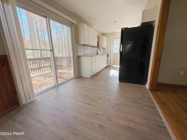 kitchen featuring backsplash, black fridge, stainless steel dishwasher, light hardwood / wood-style flooring, and white cabinets