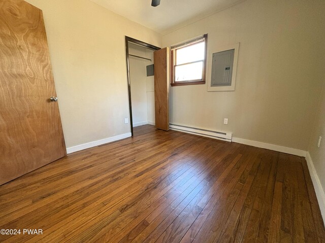 unfurnished bedroom featuring electric panel, ceiling fan, a baseboard radiator, wood-type flooring, and a closet