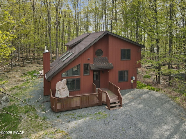 chalet / cabin featuring a wooded view, roof with shingles, a chimney, and a deck