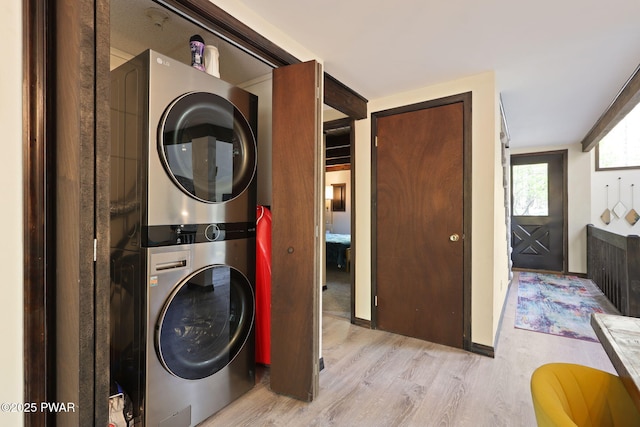 washroom featuring baseboards, laundry area, light wood finished floors, and stacked washer / dryer