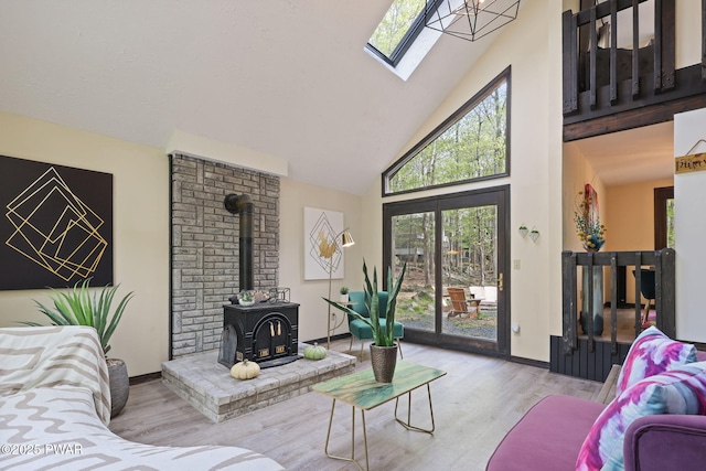 living area with a wood stove, high vaulted ceiling, baseboards, wood finished floors, and a skylight