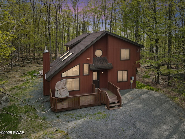 chalet / cabin with a shingled roof, a chimney, and a deck