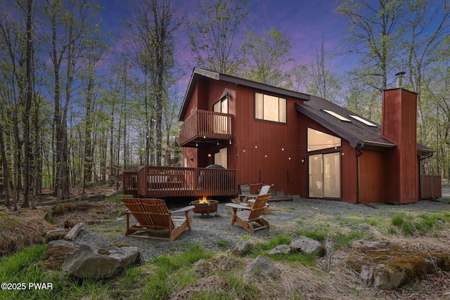 back of property featuring a deck, a chimney, a balcony, and an outdoor fire pit
