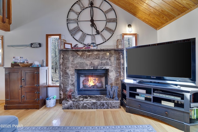 living room with wooden ceiling, a stone fireplace, wood finished floors, and lofted ceiling