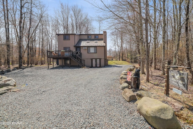 view of front of house with stairway, a wooden deck, metal roof, and a chimney