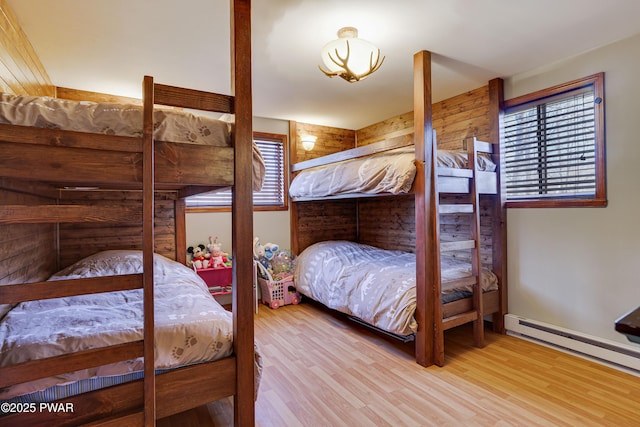 bedroom featuring a baseboard heating unit, wood finished floors, and multiple windows