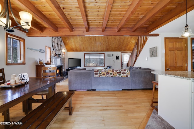 living room featuring a lit fireplace, stairway, light wood-type flooring, a chandelier, and wooden ceiling