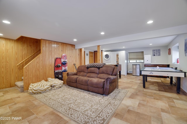 living room with wood walls, stacked washer / dryer, stairway, recessed lighting, and stone finish flooring