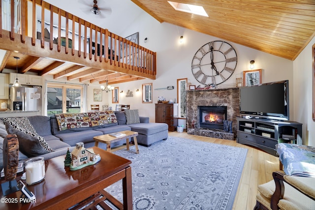 living area featuring a fireplace, high vaulted ceiling, wooden ceiling, light wood finished floors, and ceiling fan with notable chandelier
