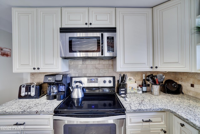 kitchen featuring decorative backsplash, white cabinetry, light stone countertops, and stainless steel appliances