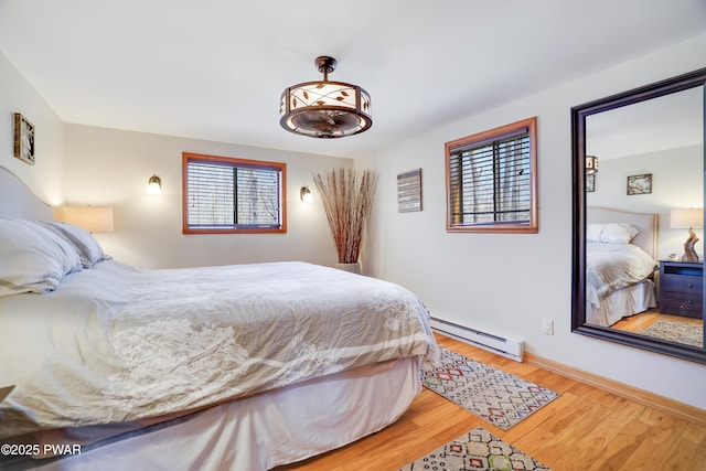 bedroom with baseboards, a baseboard heating unit, and light wood finished floors