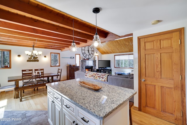 kitchen featuring a warm lit fireplace, light stone counters, a center island, beamed ceiling, and pendant lighting