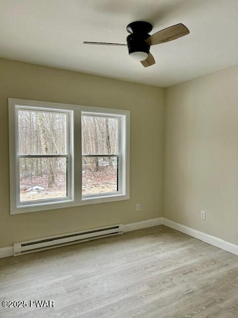 empty room featuring ceiling fan, light hardwood / wood-style floors, and a baseboard heating unit