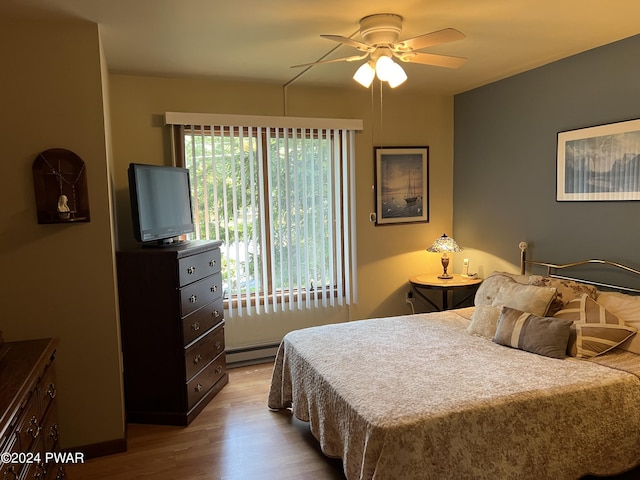 bedroom featuring ceiling fan, light hardwood / wood-style flooring, and a baseboard heating unit