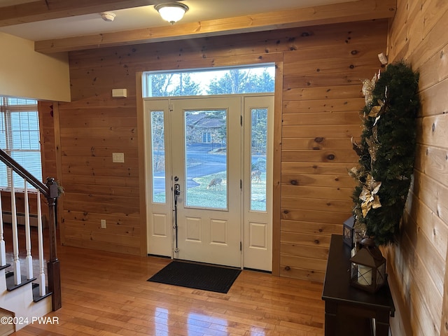 foyer entrance featuring beam ceiling, light wood-type flooring, a baseboard radiator, and wood walls