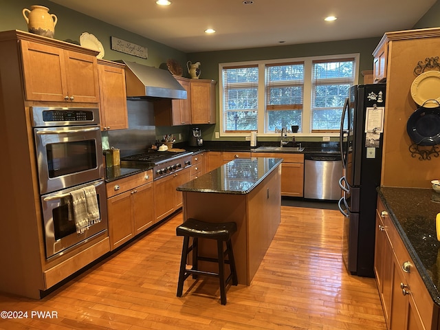 kitchen featuring a center island, stainless steel appliances, dark stone counters, and wall chimney range hood