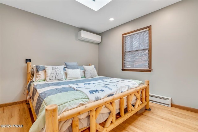 bedroom with baseboard heating, a wall mounted AC, light hardwood / wood-style flooring, and a skylight