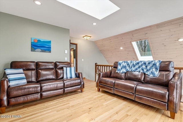 living room featuring wooden walls, light hardwood / wood-style flooring, and vaulted ceiling with skylight