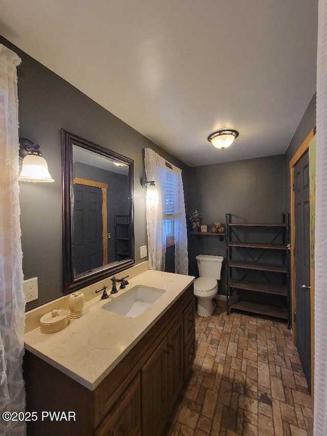 bathroom with brick floor, vanity, and toilet