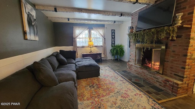 living room featuring beam ceiling, a wainscoted wall, a brick fireplace, brick wall, and wood finished floors