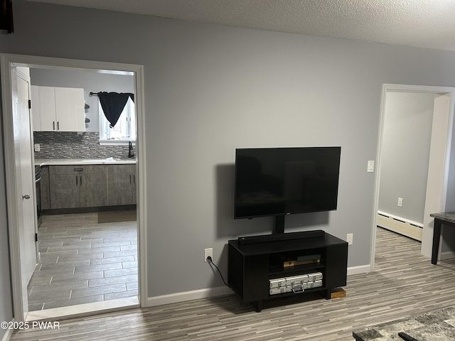 living room with light wood-type flooring, a baseboard radiator, baseboards, and a textured ceiling