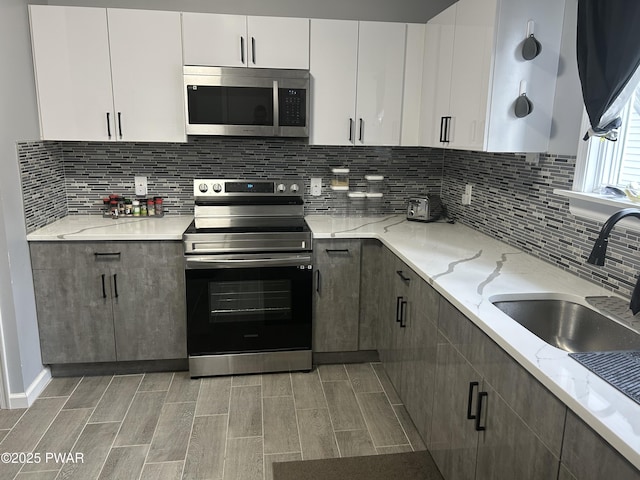 kitchen with tasteful backsplash, appliances with stainless steel finishes, white cabinets, and a sink