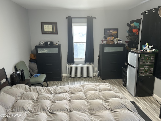 bedroom with light wood-type flooring, freestanding refrigerator, baseboards, and radiator heating unit