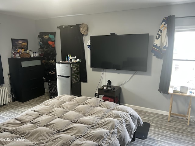 bedroom with freestanding refrigerator, radiator heating unit, baseboards, and wood finished floors