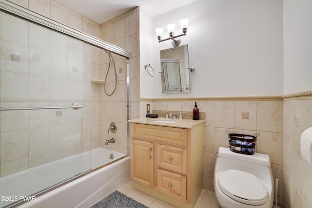 full bath featuring a wainscoted wall, toilet, vanity, enclosed tub / shower combo, and tile walls