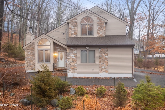 view of front of property featuring a chimney, stone siding, and a shingled roof