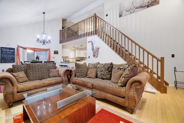 living area with hardwood / wood-style floors, stairway, high vaulted ceiling, an inviting chandelier, and beamed ceiling