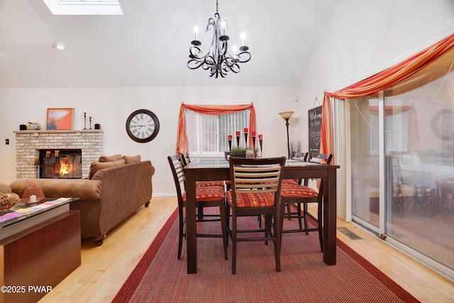 dining room featuring visible vents, lofted ceiling with skylight, wood finished floors, an inviting chandelier, and a fireplace