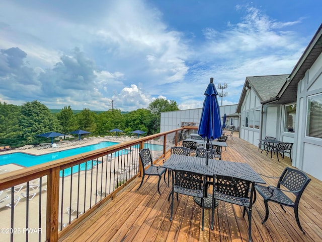 wooden deck with outdoor dining area and a community pool