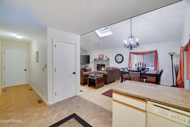 kitchen with light tile patterned floors, hanging light fixtures, dishwasher, lofted ceiling with skylight, and a brick fireplace