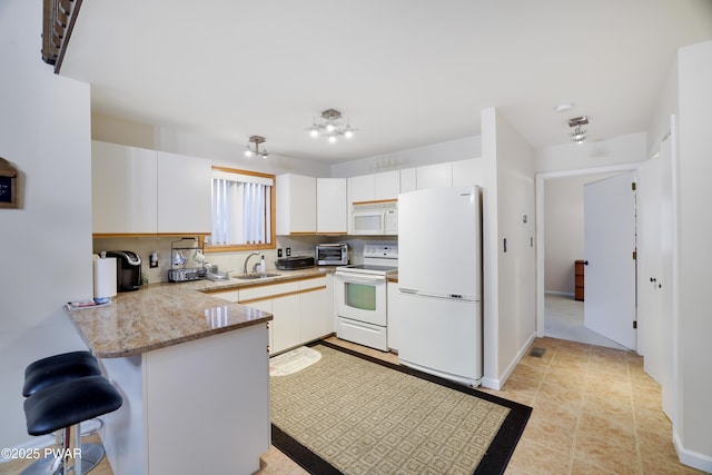 kitchen with a toaster, a breakfast bar, a peninsula, white appliances, and a sink