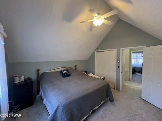 bedroom featuring a textured ceiling, a closet, lofted ceiling, light colored carpet, and ceiling fan