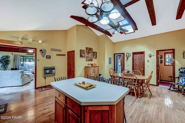 kitchen featuring ceiling fan, vaulted ceiling with beams, heating unit, light hardwood / wood-style floors, and a kitchen island