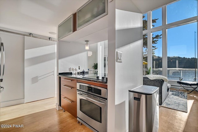 kitchen with black electric stovetop, light wood-type flooring, oven, and plenty of natural light