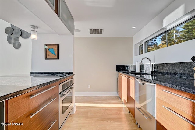 kitchen with pendant lighting, stainless steel oven, sink, and dark stone counters