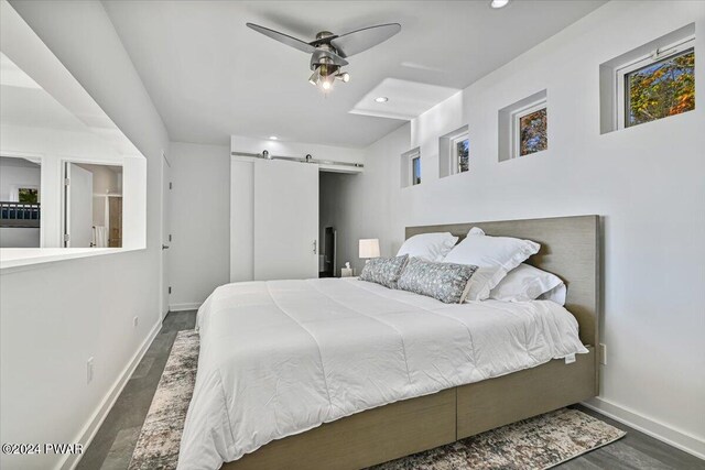 bedroom with a barn door, ceiling fan, and dark hardwood / wood-style flooring