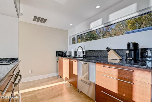 kitchen with sink, light hardwood / wood-style flooring, a wealth of natural light, and dark stone counters